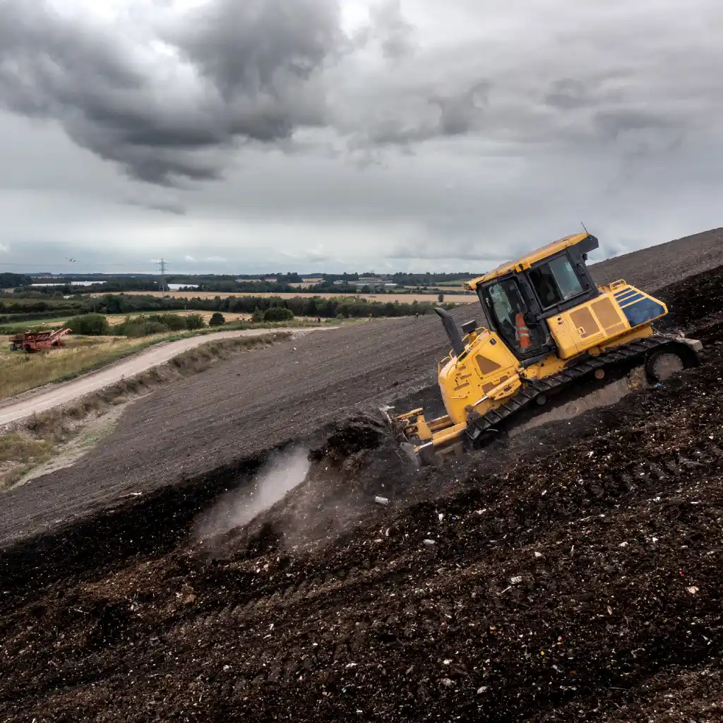 A yellow bulldozer on a slope moving waste on a landfill site in the UK